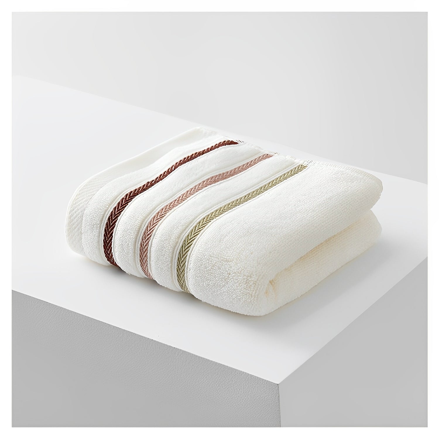 Elevkassan Handduk med Ränder - Beige är en vikt vit handduk med tre broderade chevronränder i brunt, beige och olivgrönt, tillverkad av absorberande frottématerial och placerad på en vit yta med en minimalistisk bakgrund.